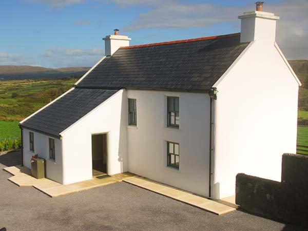 a small white house with a black roof at Nellie's Farmhouse in Bantry