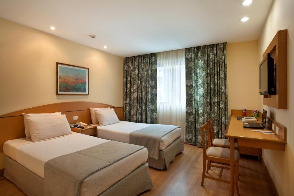 a hotel room with two beds and a desk at Windsor Martinique Copacabana in Rio de Janeiro