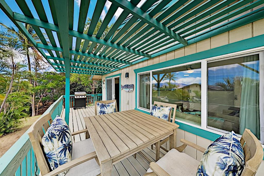 un patio con una mesa de madera y sillas en una terraza en Nahenahe Cottage, en Wailea