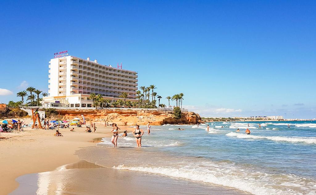 a beach with people in the water and a building at La Zenia Beach House in Alicante