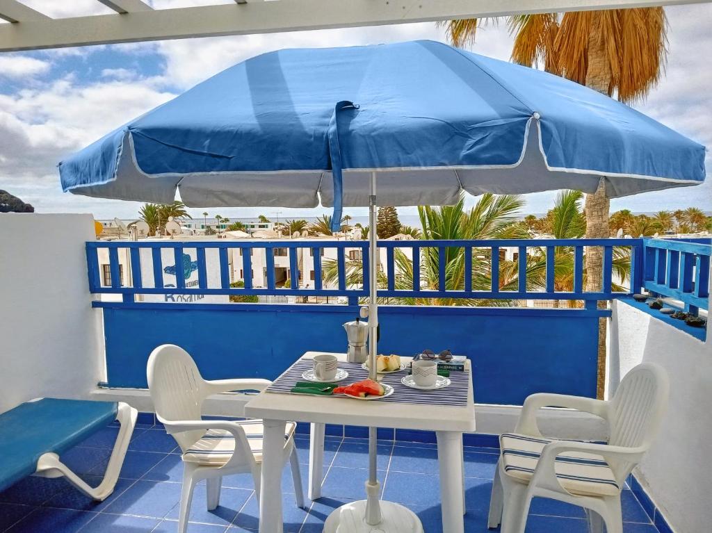 a table and chairs under a blue umbrella on a balcony at Aguazul - A pie de piscina y vistas al mar in Puerto del Carmen