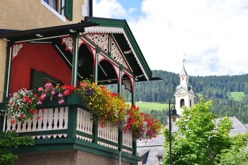 a balcony with flowers on a building with a church at Aurturist Villabassa in Villabassa