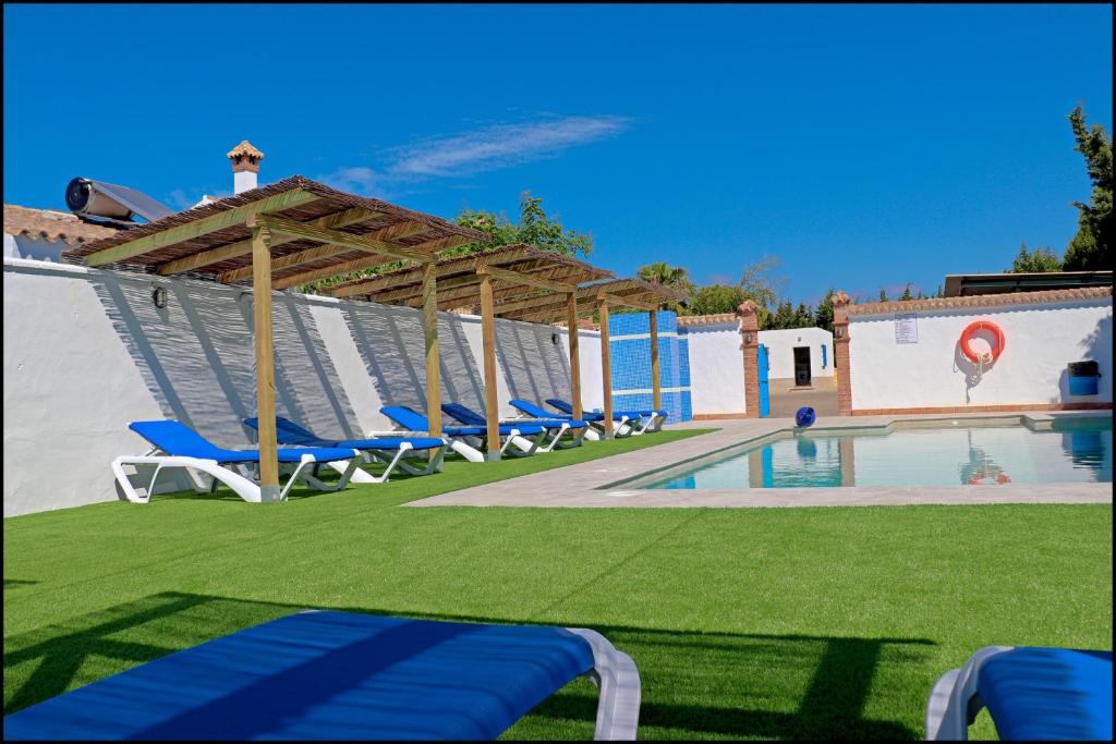 a swimming pool with blue chairs and a pavilion at Bungalow La Roa IV in Conil de la Frontera
