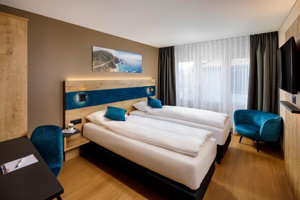 two beds in a hotel room with blue chairs at Hotel California in Zurich