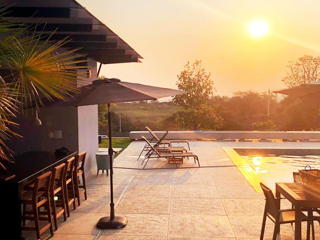 eine Terrasse mit Tischen, Stühlen und einem Sonnenschirm in der Unterkunft Casa com piscina aquecida e churrasqueira em Itu in Aparecida