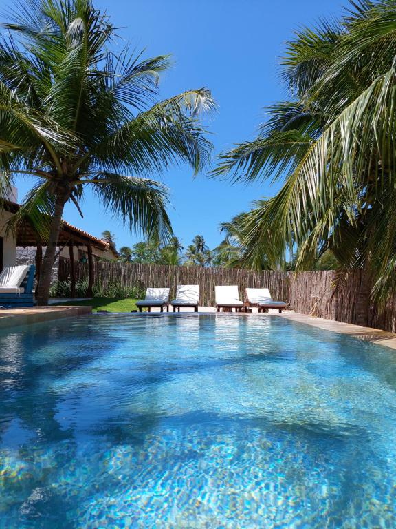 uma piscina com duas cadeiras e palmeiras em Villa Aracoara em Praia do Preá