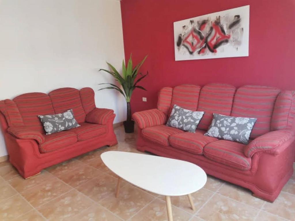una sala de estar con 2 sofás rojos y una mesa. en Apto Playa Camelle 1º en Camelle