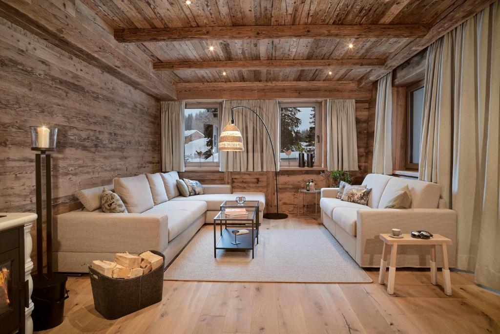 a living room with two white couches and a wooden wall at Berghaus Schröcken - Hotel Apartments Spa in Schröcken