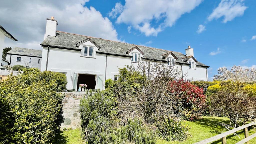 a white house with a dog sitting in the doorway at Orchard Cottage - Walking distance of the river, charming sunny patio, quiet location in Dittisham