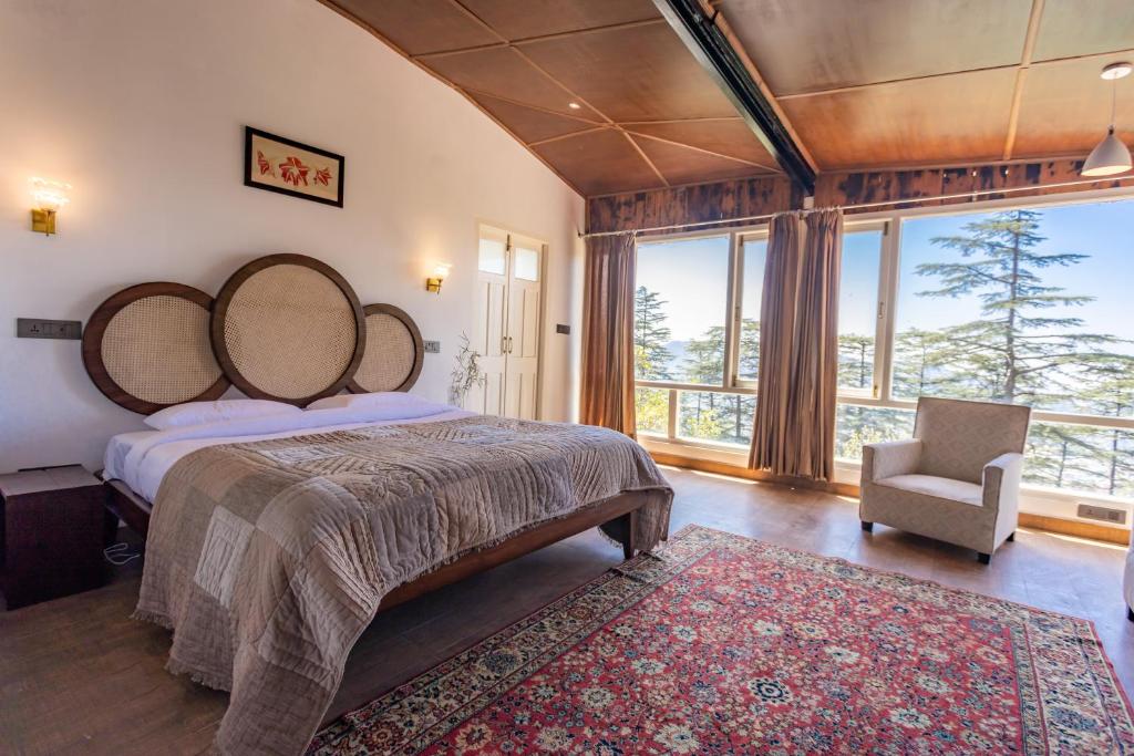 a bedroom with a large bed and a chair and windows at Seclude Shimla, Taraview in Shimla