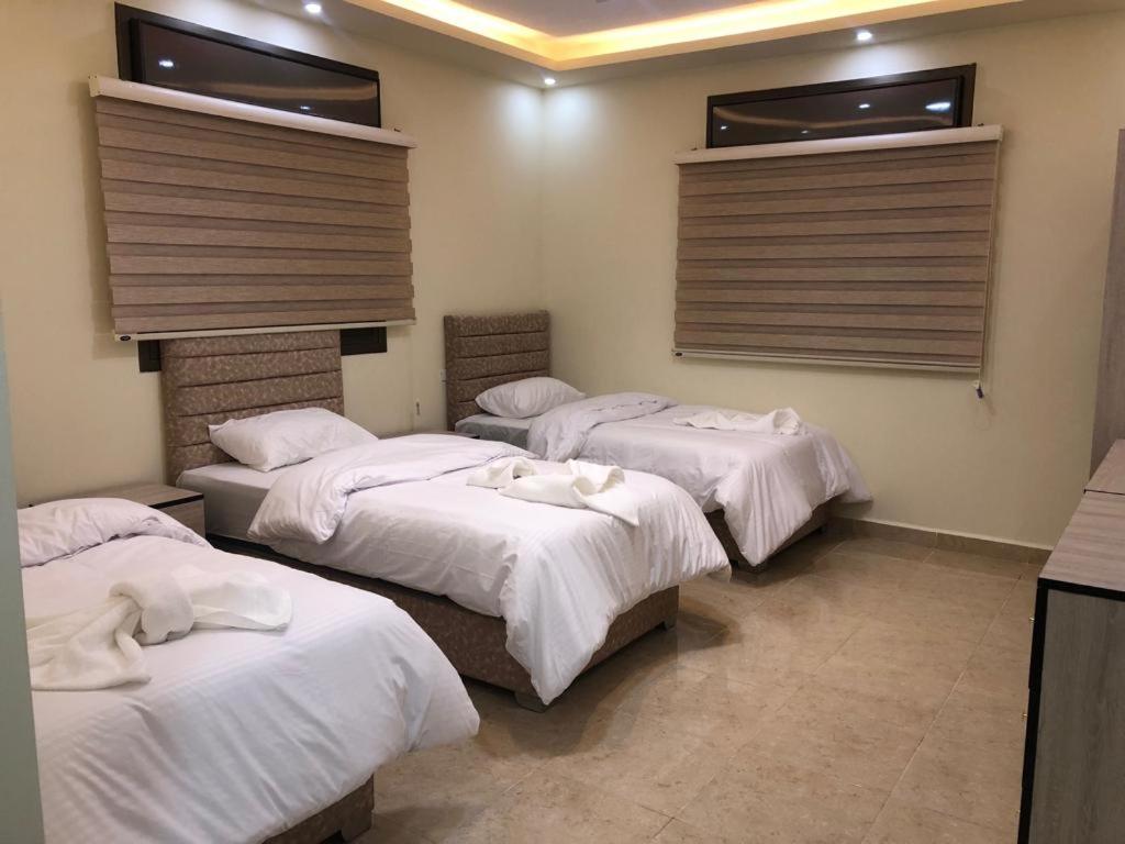 a room with four beds with white sheets and windows at Authentic boutique in Wadi Musa