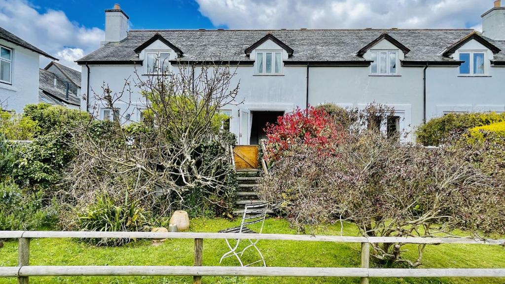 a white house with a fence in front of it at Damson Cottage - Peaceful location, charming communal orchard & private patio garden in Dittisham
