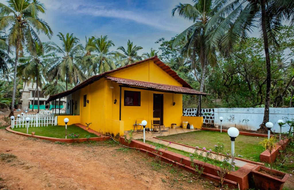 een geel huis in een veld met palmbomen bij Vinsons Cottages in Colva