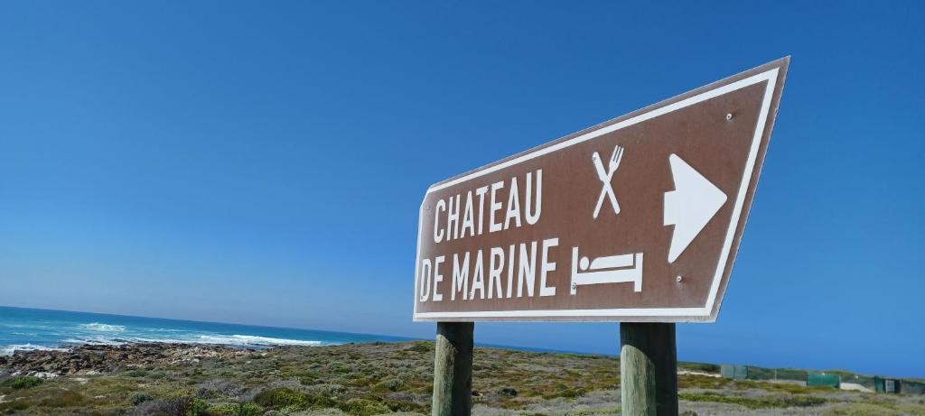 un cartel en la playa con el océano en el fondo en Chateau de Marine Boutique Hotel, en Struisbaai