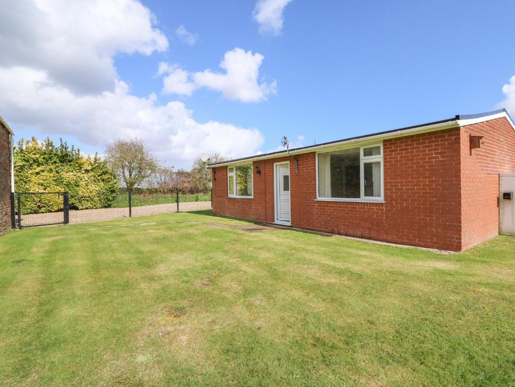 a red brick house with a grass yard at Sheppard's Hut in Terrington Saint Clement