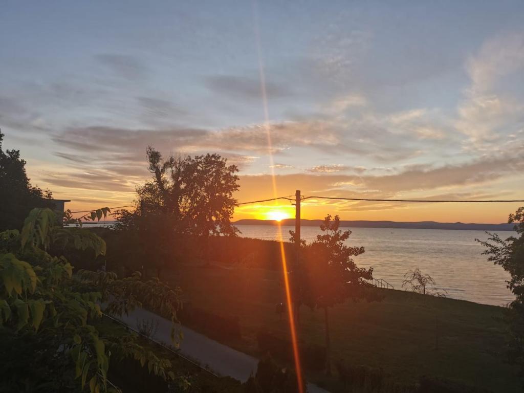 una puesta de sol sobre un cuerpo de agua con un poste en Traumlage direkt am See, en Balatonszemes