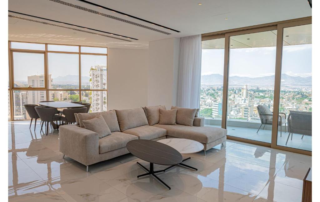 360 Nicosia - Luxury Apartment Panoramic View في نيقوسيا: غرفة معيشة مع أريكة وطاولات ونوافذ