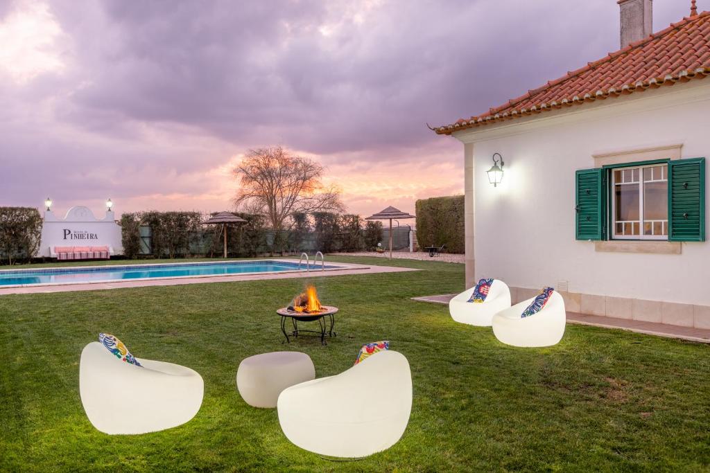 Alpiarça的住宿－Quinta da Pinheira Lezíria，后院设有四把白色椅子和一个火坑