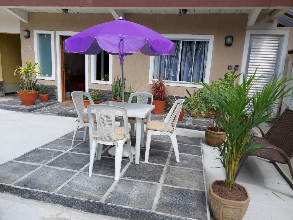 uma mesa e cadeiras com um guarda-chuva roxo em Itaúna Surf Beach em Saquarema