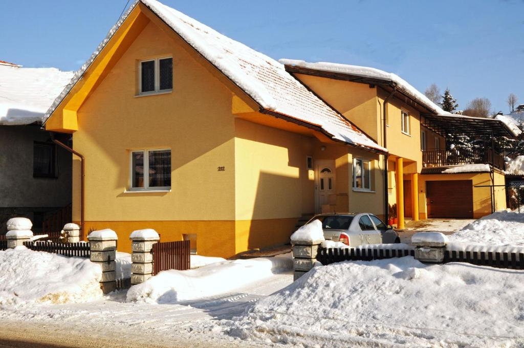 una casa amarilla con un coche aparcado en la nieve en Ubytovanie v Súkromi Habovka, en Habovka