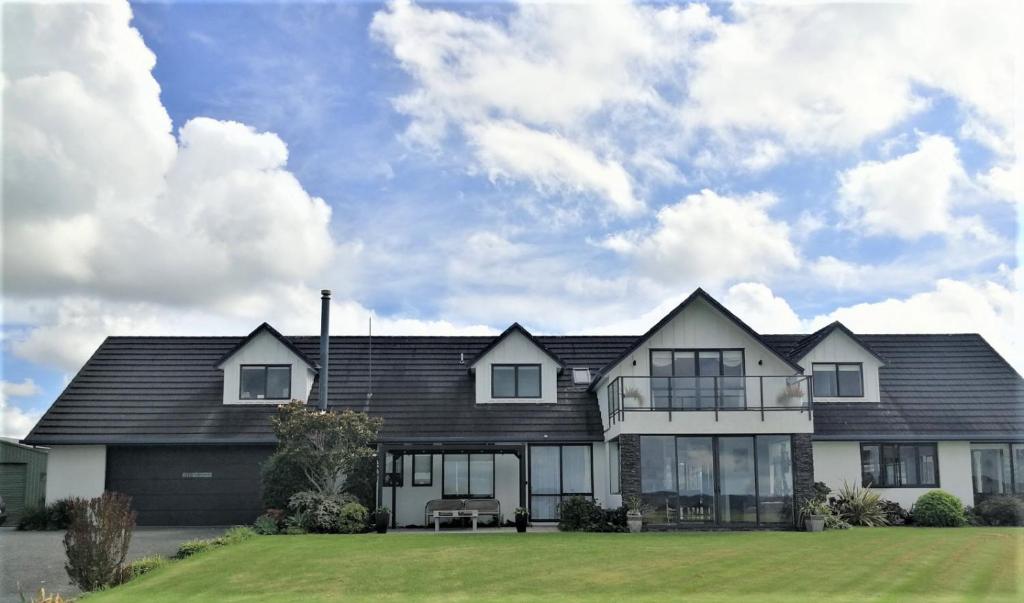 a house with a black roof and a green yard at Kaka Lodge at Kotare House in Tawharanui