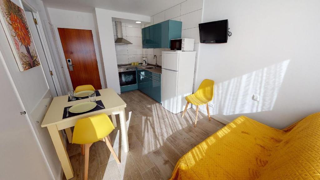 a small kitchen with a table and yellow chairs at Apartamentos Eldorado in Lloret de Mar