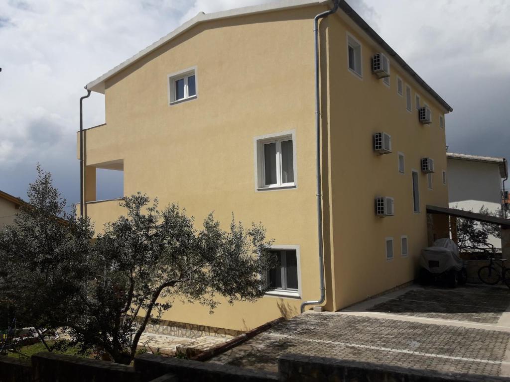 un edificio amarillo con un árbol delante de él en Apartments Marijan, en Pirovac