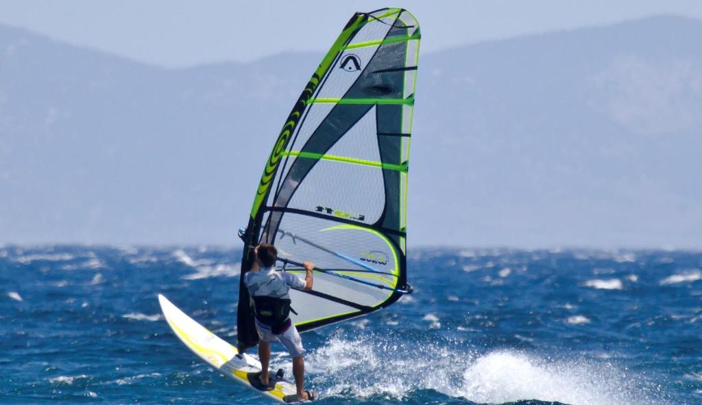mężczyzna na desce surfingowej z żaglem na oceanie w obiekcie Ballos Apartments w mieście Nea Makri