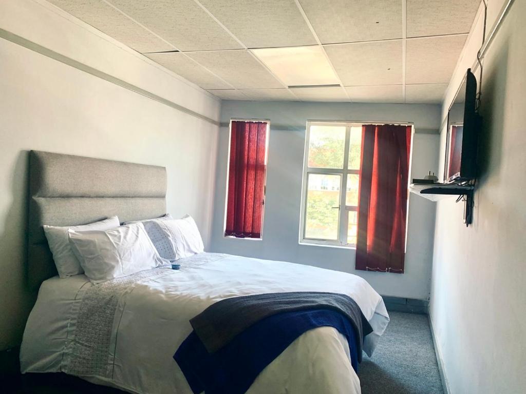 a bedroom with a bed and two windows with red curtains at Stay Inn Lodge Randfontein in Randfontein