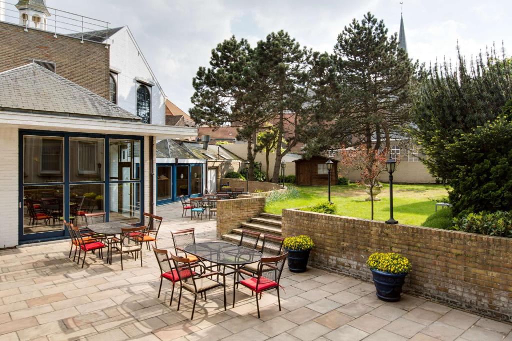 a patio with tables and chairs and a brick wall at NH Brugge in Bruges