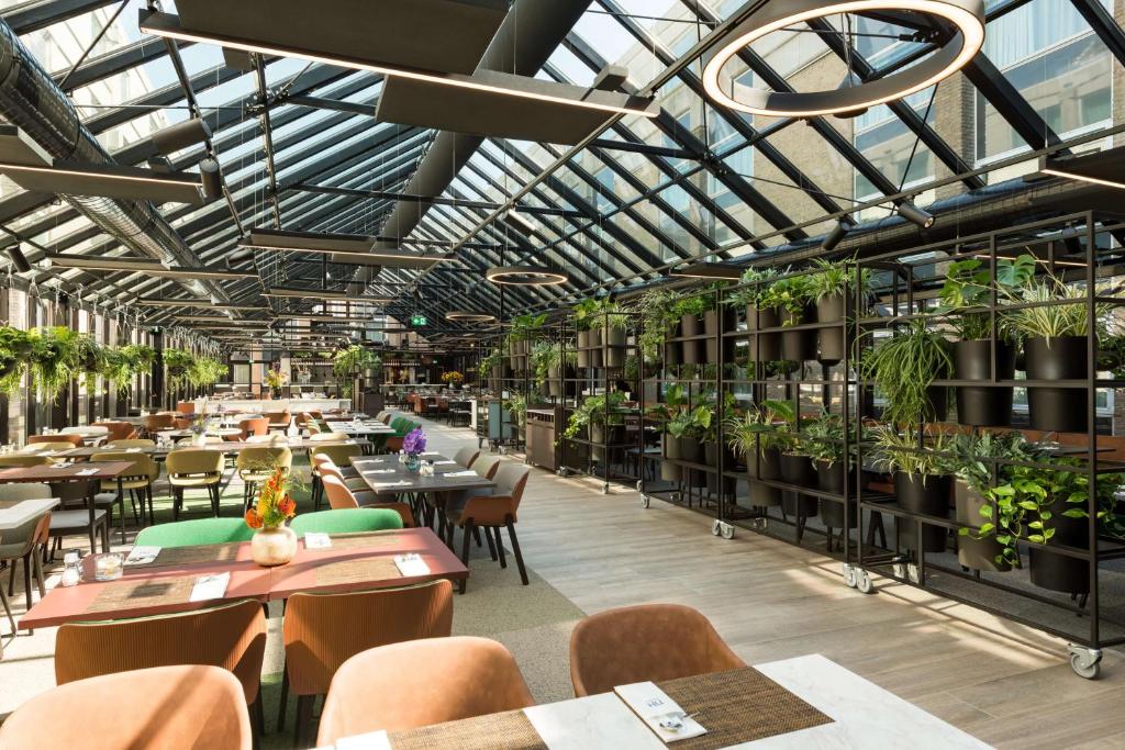 a restaurant with tables and chairs and potted plants at NH Amsterdam Schiphol Airport in Hoofddorp