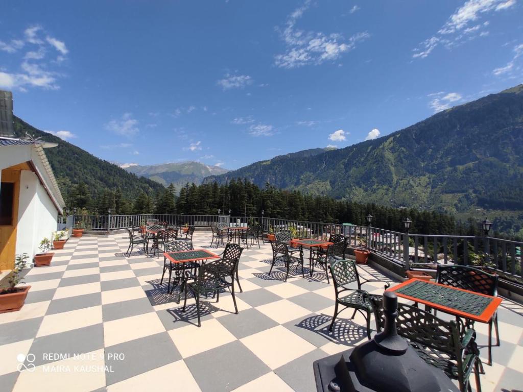 een patio met tafels en stoelen met bergen op de achtergrond bij Abhilashi Residency & Spa - Centrally Heated & Air Cooled in Manāli