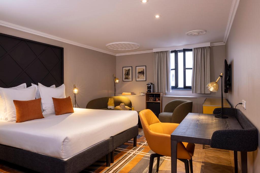 
a hotel room with a bed, chair, table and lamps at Le Colombier in Colmar
