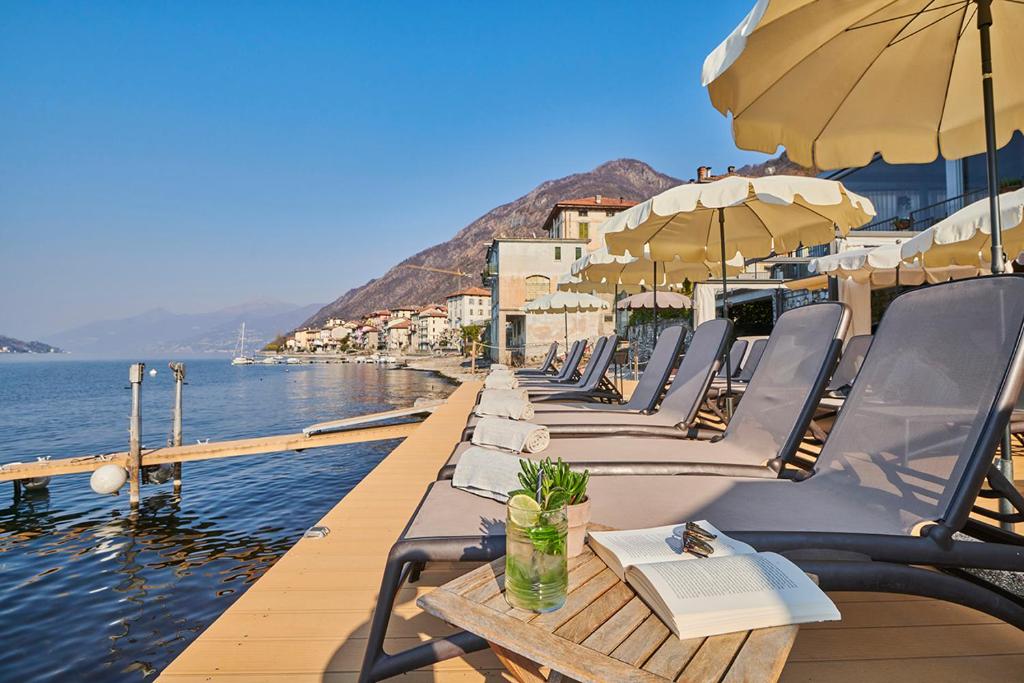 una fila de sillas y mesas con sombrillas en el agua en Hotel Villa Aurora, en Lezzeno