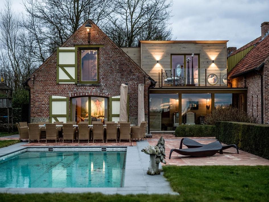 uma casa com piscina em frente a uma casa em Aan de Blankaart em Woumen