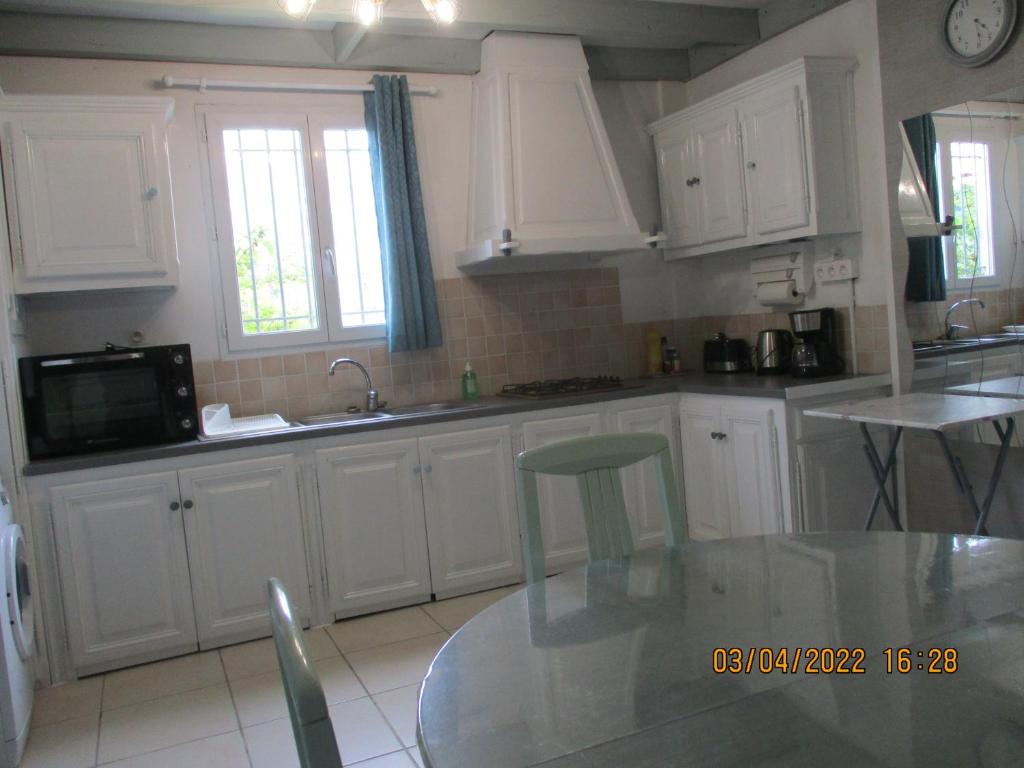 eine Küche mit weißen Schränken und einem Glastisch in der Unterkunft Le Pijolin in Saint-Justin
