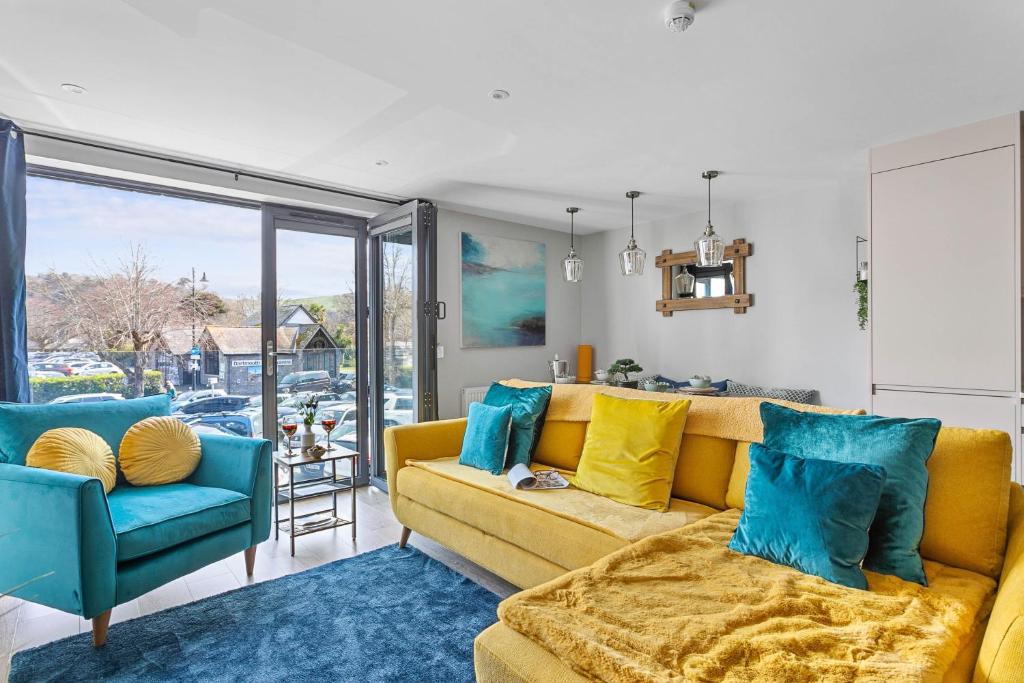 a living room with a yellow couch and blue chairs at 2 De Courcey House - Architect designed luxury apartment with parking, central Dartmouth in Dartmouth