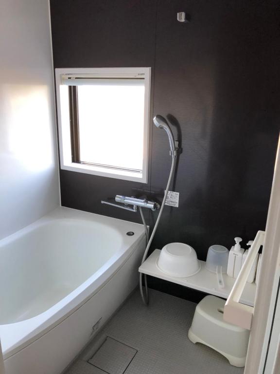 a bathroom with a tub and a toilet and a window at ゴールデンマイルヴィラ in Amami