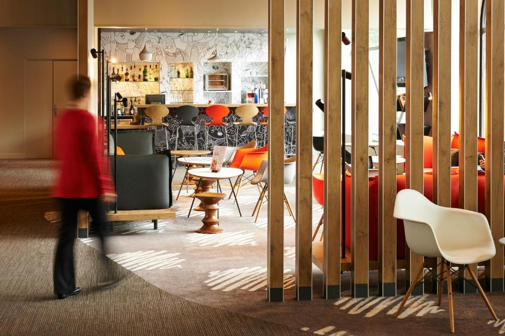 a woman walking through a restaurant with chairs and tables at ibis Strasbourg Centre Historique in Strasbourg