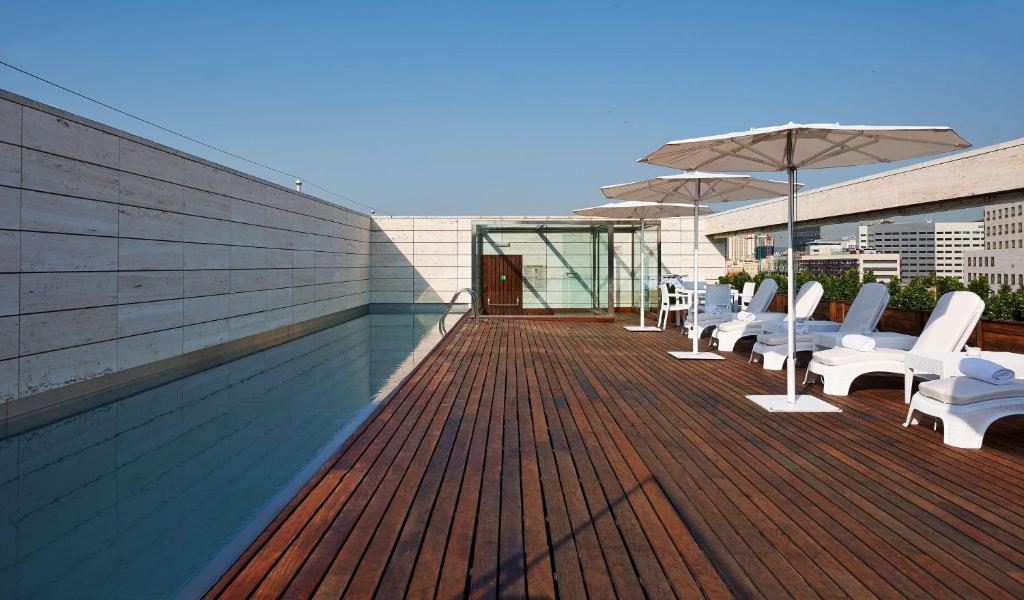 una terraza de madera con sillas blancas y sombrilla en NH Collection Barcelona Constanza, en Barcelona