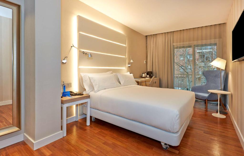 Schlafzimmer mit einem großen weißen Bett und einem Schreibtisch in der Unterkunft NH Barcelona Les Corts in Barcelona