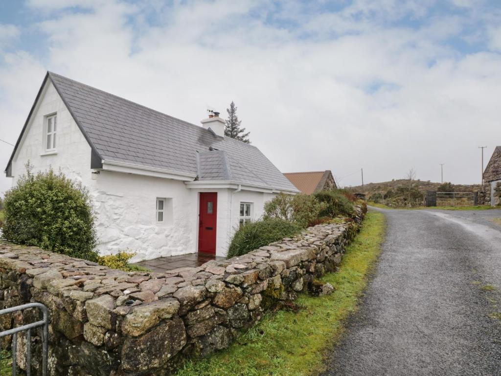 uma casa branca com uma parede de pedra ao lado de uma estrada em Tigh Mhicïl em Glentrasna