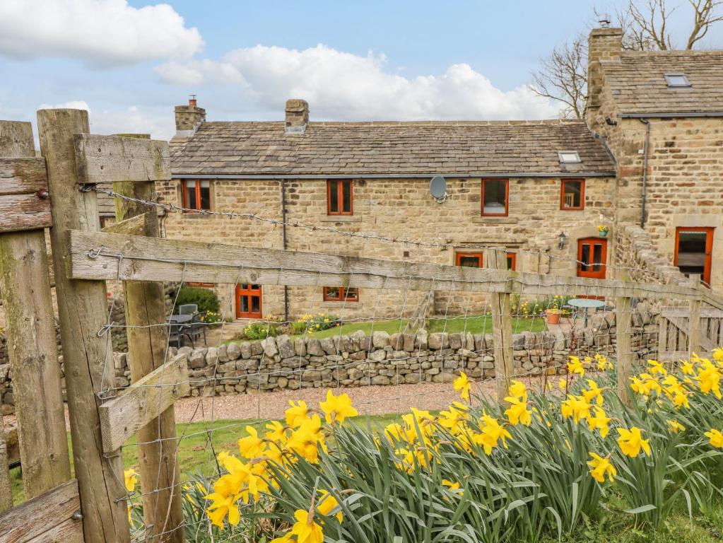 an old stone house with a fence and yellow flowers at Curlew Cottage in Keighley
