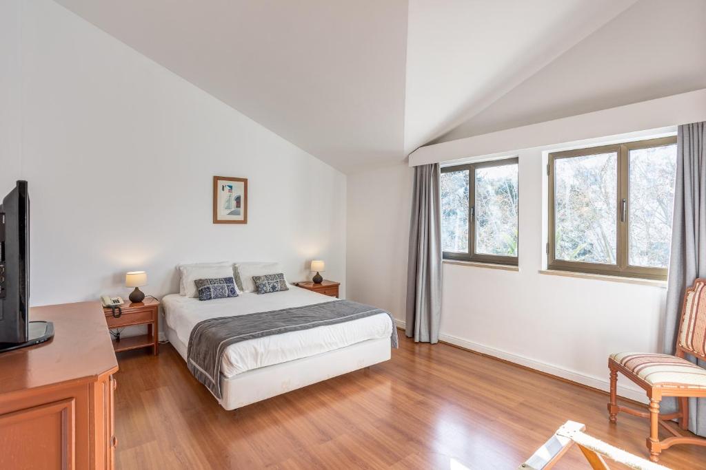 een slaapkamer met een bed, een bureau en ramen bij Clube do Lago Hotel in Estoril