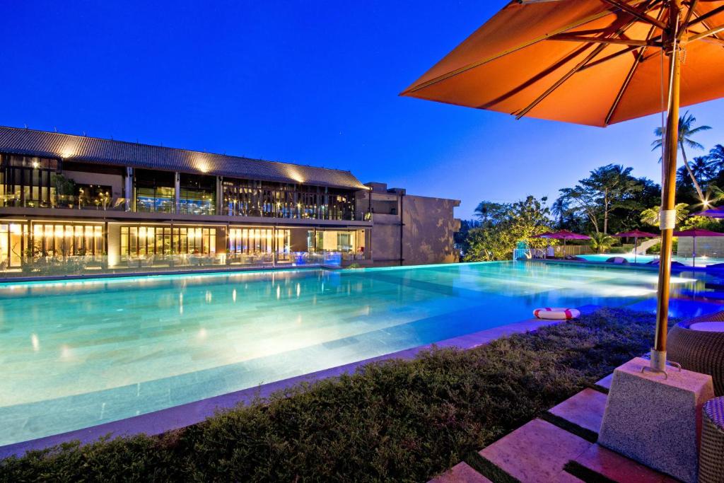 a swimming pool with an umbrella in front of a building at Sunsuri Phuket - SHA Plus in Nai Harn Beach