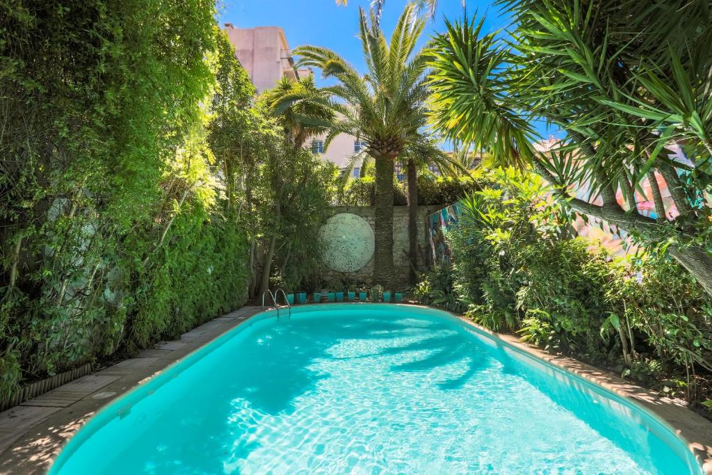 a swimming pool in a garden with palm trees at Le Windsor, Jungle Art Hotel in Nice