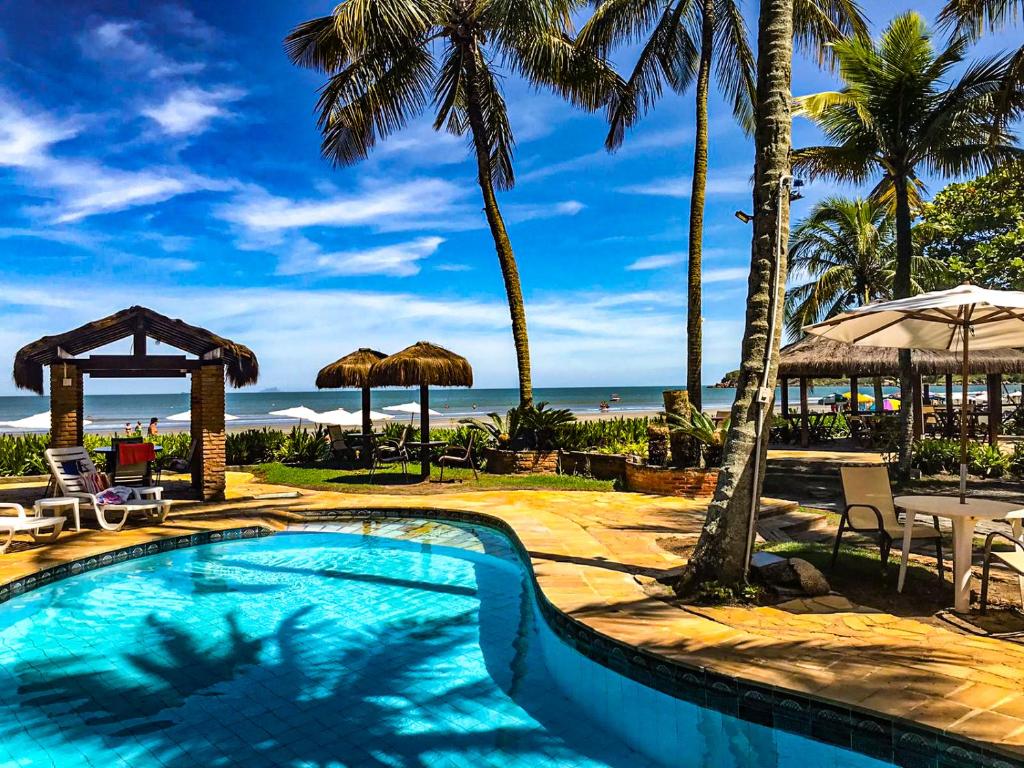 una piscina con palmeras y el océano en Barequeçaba Praia Hotel, en Barequeçaba