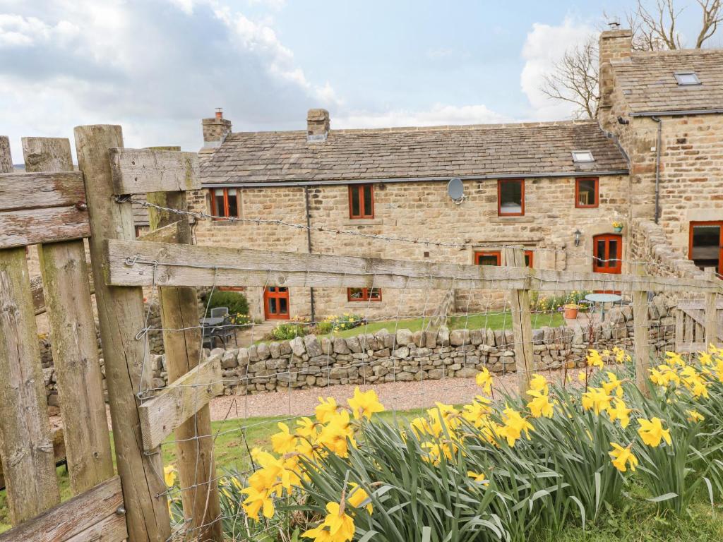 an old stone house with a fence and yellow flowers at Kestrel Cottage in Keighley