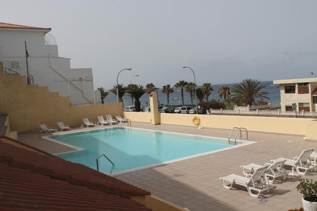 a large swimming pool with lounge chairs and the ocean at Apartamento Playa vistas 2 in Los Cristianos
