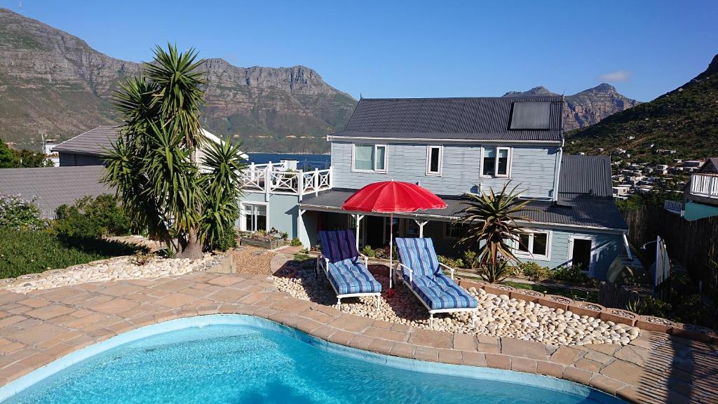 a house with a swimming pool with two chairs and a red umbrella at Villa Amanzi in Hout Bay